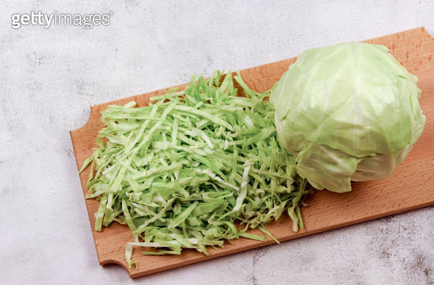 Young cabbage head and shredded cabbage on a wooden cutting board on a ...