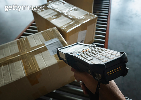 Worker scanning barcode scanner with cargo boxes on conveyor belt ...