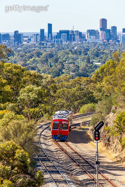 Red diesel short passenger train heads through hills towards city in ...