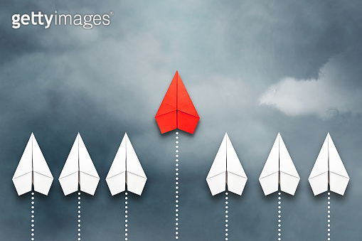 Red paper plane flying in front of a group of whites. Cloudy sky ...