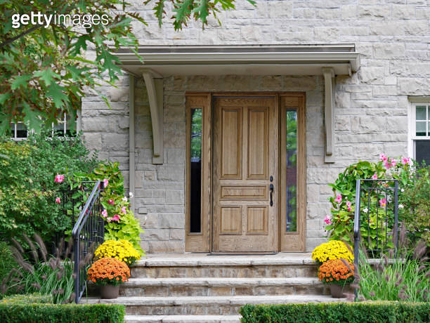 Front steps of stone house with wood grain front door and flower pots ...