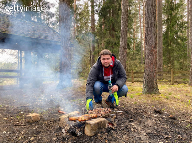A man roasts pork and chicken shish kebab on a campfire in nature ...