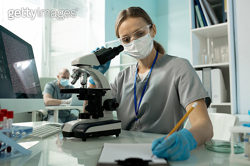 Female laboratory worker making notes in document while working with ...