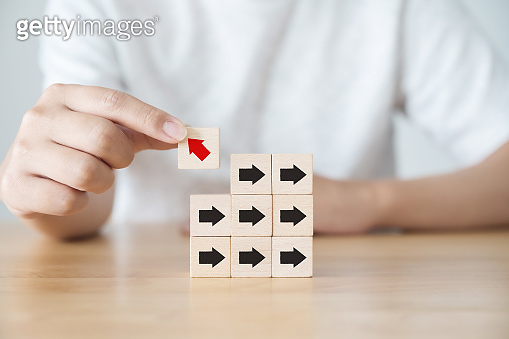 Hand holding wooden block with red arrow facing the opposite direction ...