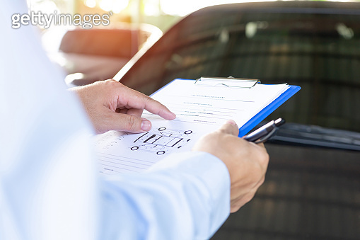Insurance agent check on clipboard while examining car after accident ...