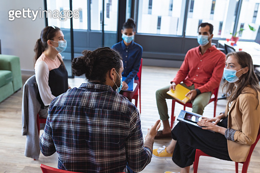 Diverse group of creative colleagues wearing face masks talking at ...