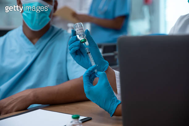 Mixtet Injection Mixed race couple of doctors wearing face masks preparing to make ...