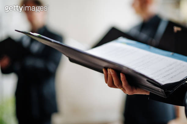 Hand holds notes during choir rehearsal and scrolls, shallow depth of ...