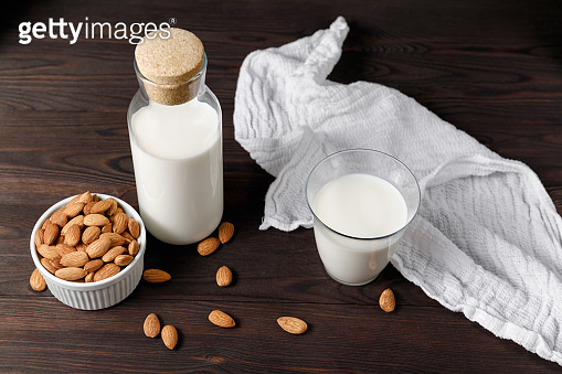 Almond milk in a glass and a glass bottle on dark wooden background