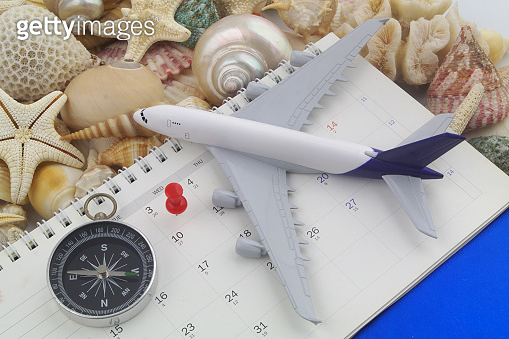 Airplane, compass and push pin on calendar on many seashells ...