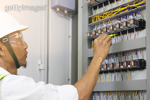 A male electrician works in a control panel with electrical connections ...