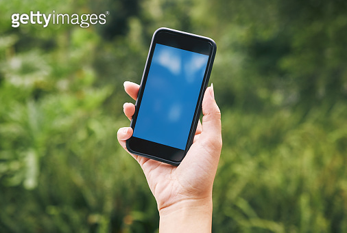 A hand holding a cellphone outside in nature. A mobile phone devise in ...