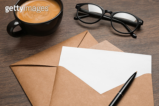 Envelopes with blank paper card, cup of coffee, glasses and pen on ...