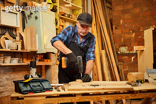 Portrait of a senior carpenter with drilling instrument working in the ...