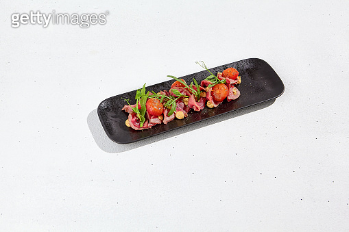 Roast beef with cherry tomatoes, ruccola and spicy sauce on black plate ...