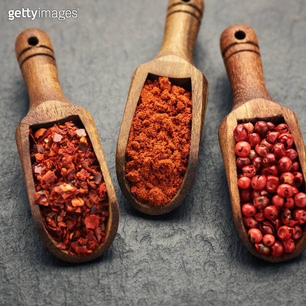 Crushed pepper, paprika, peppercorn and cayenne in wooden spoons over