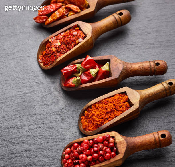 Crushed pepper, paprika, peppercorn and cayenne in wooden spoons over