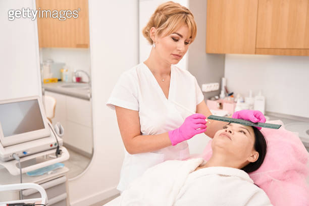 Female esthetician uses special pencil and ruler to mark eyebrows ...