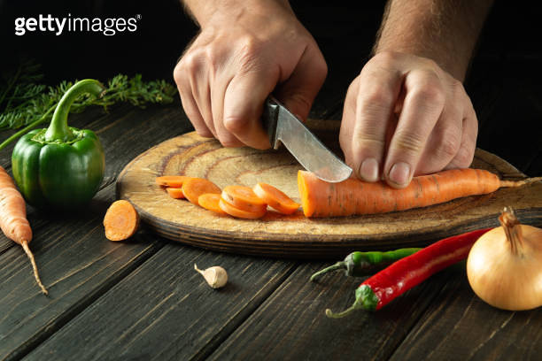 The cook cuts carrot into small pieces on a cutting board for preparing ...