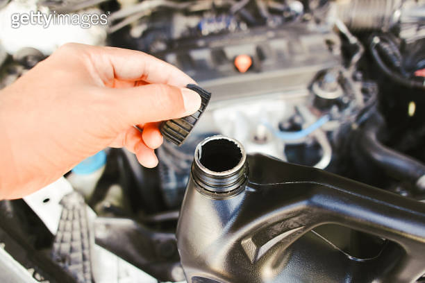 The hand of a car mechanic opens the engine oil cap to inspect before ...