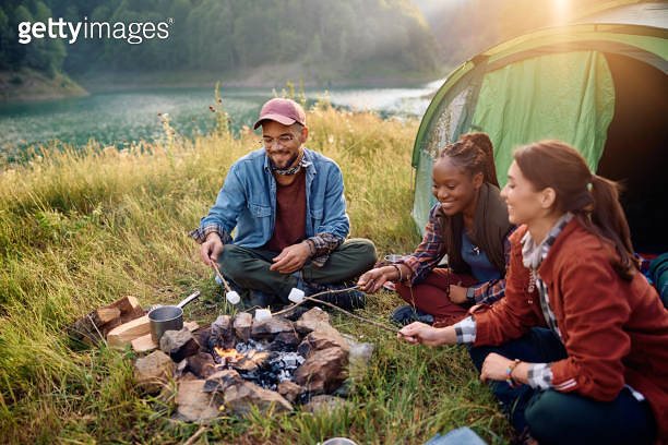 Young happy friends roasting marshmallows above campfire in nature. 이미지 ...