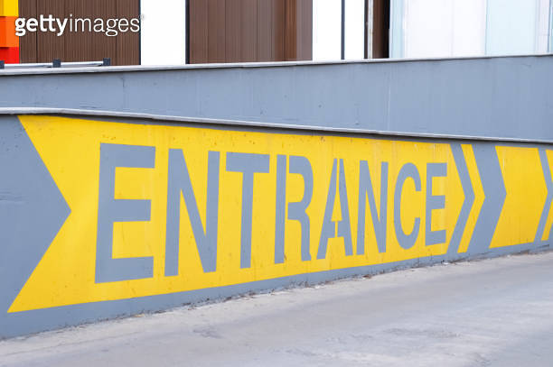 Entrance yellow sign with direction arrows printed on the gray concrete ...