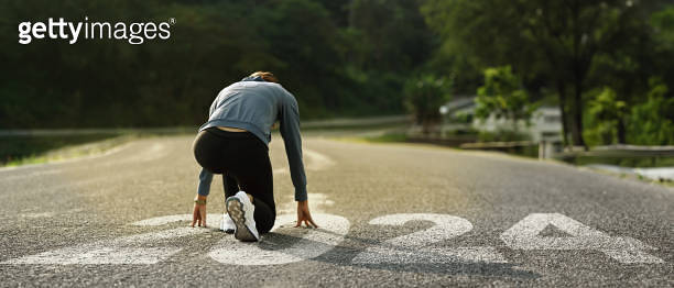 Back view of female runner in starting position on road with numbers ...