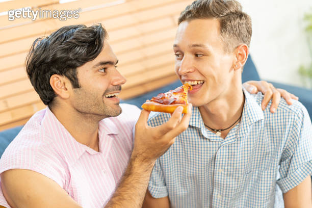 Cheerful Gay Couple Eating Pizza Gay Couple Sitting On Sofa At Home