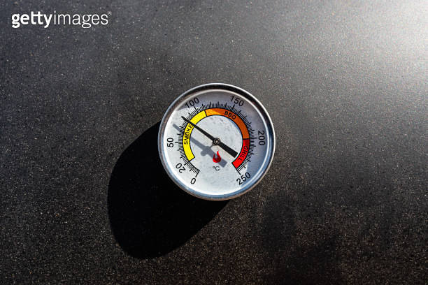 A round thermometer showing 80 degrees Celsius placed on a charcoal ...