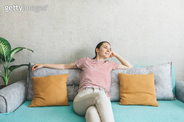 A relaxed young woman is sitting on the couch at home. Well-being, rest ...