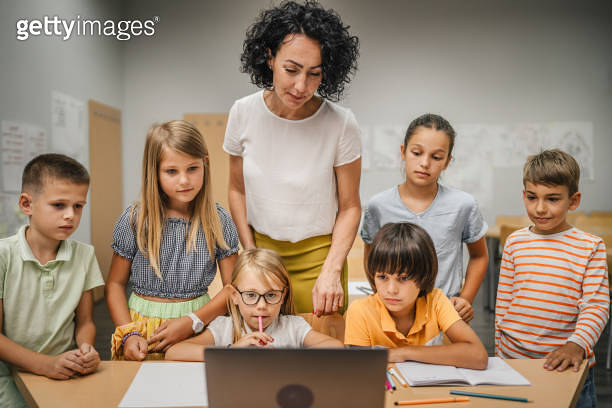 Mature teacher teach her students how to use laptop in the classroom ...