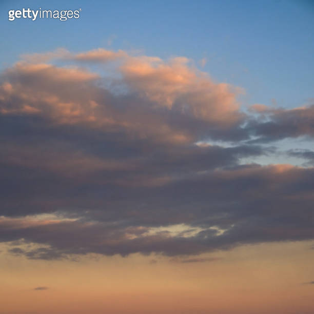 A serene sky with gentle clouds, illuminated by the fading sunlight ...