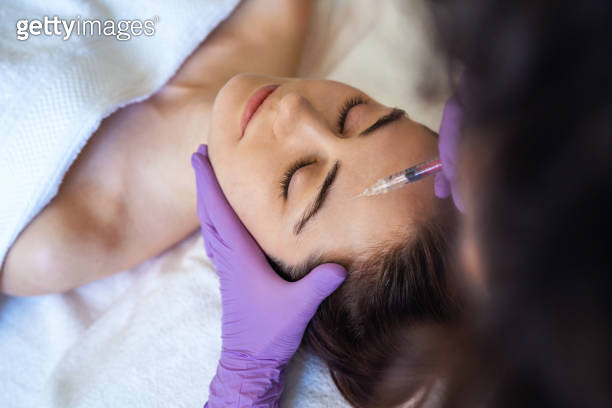 Hand Injecting Botox Doctor's hands in purple gloves injecting botox on woman face for anti ...