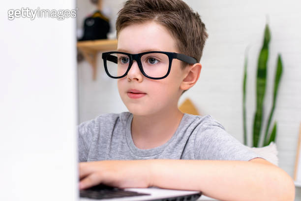 Close up of a serious smart boy works at a laptop for his new project ...