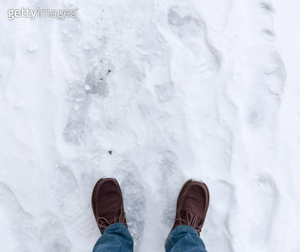 feet-in-boots-on-asphalt-covered-with-snow-1922941150