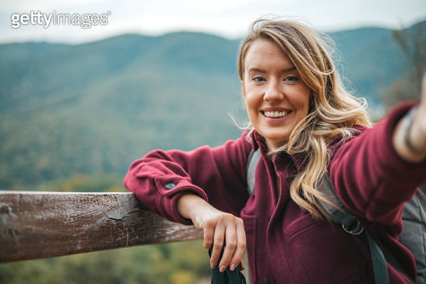Portrait of a young female hiker taking a selfie high on mountain in ...