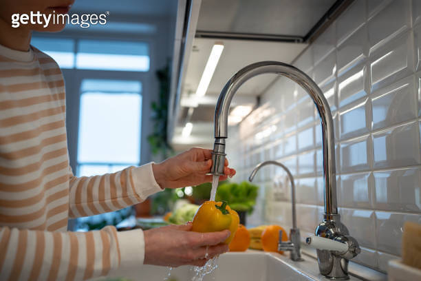 Hands washing fresh yellow pepper under tap water. Cooking dinner of ...