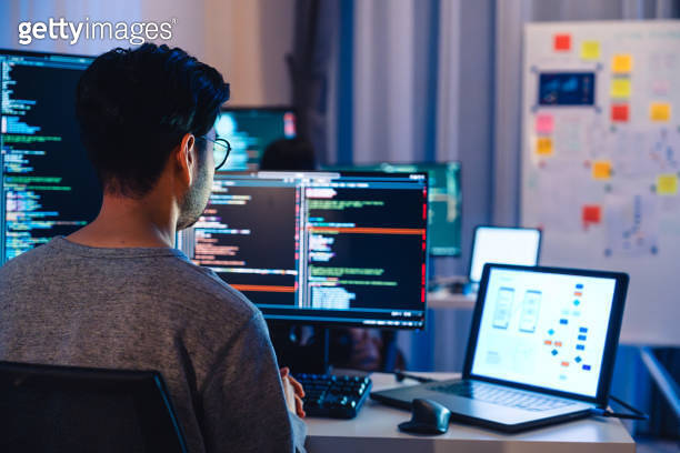 Asian software developers working on multiple screens displaying code ...