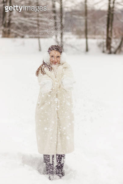 Happy young woman in a white fur coat, mittens and fur headphones on a ...