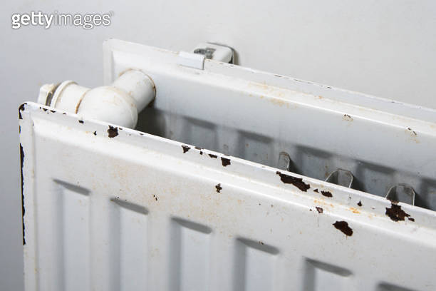 A radiator in the room has rust protruding from its white paint ...