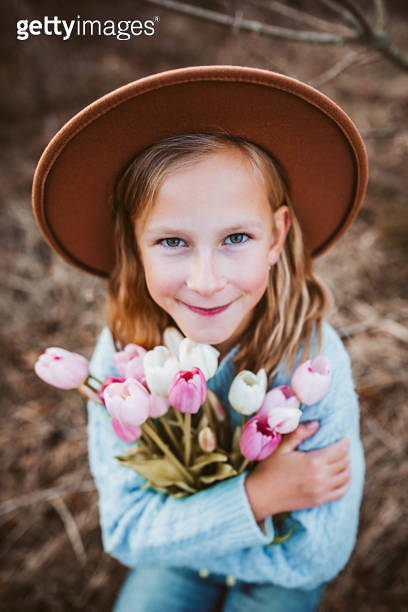 Portrait of a beautiful girl with a hat, holding bouquet of pink tulips ...
